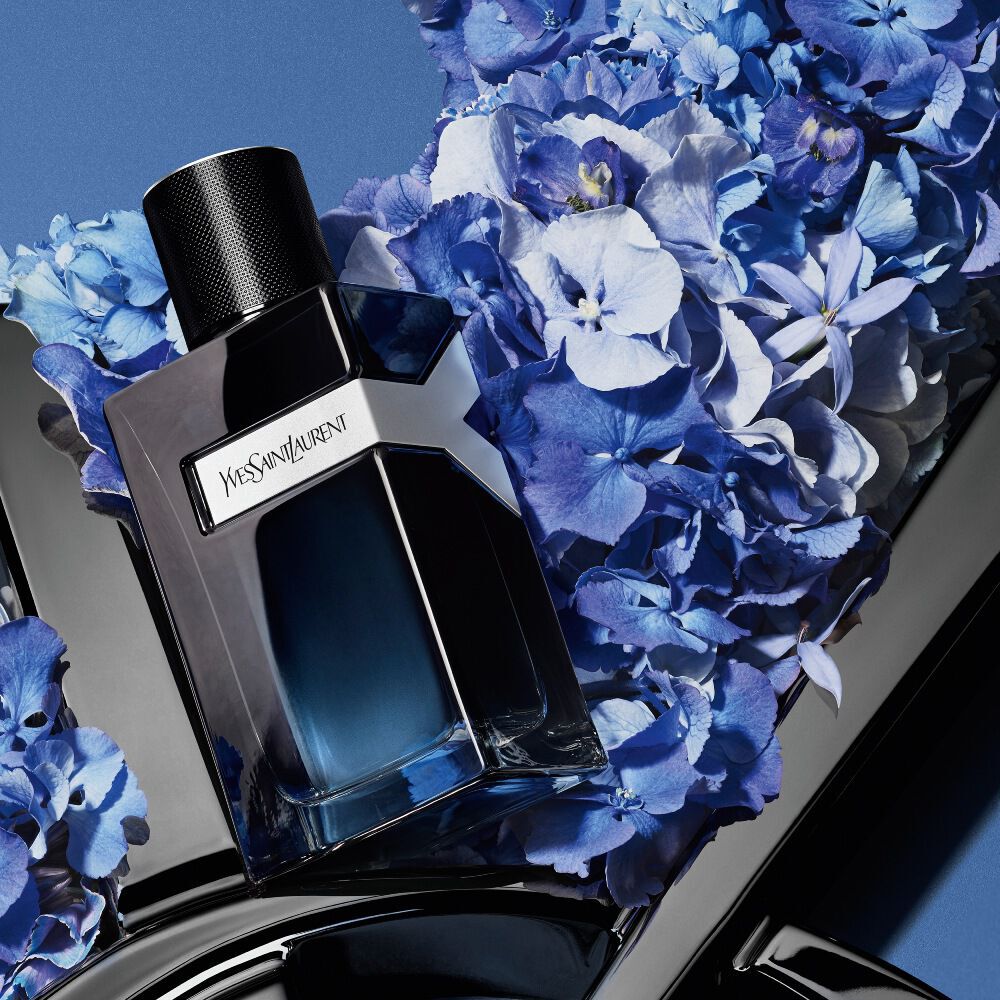 Botella de YSL Y Eau de Parfum sobre el logotipo negro brillante de YSL, rodeada de vibrantes hortensias azules, con un fondo azul profundo.