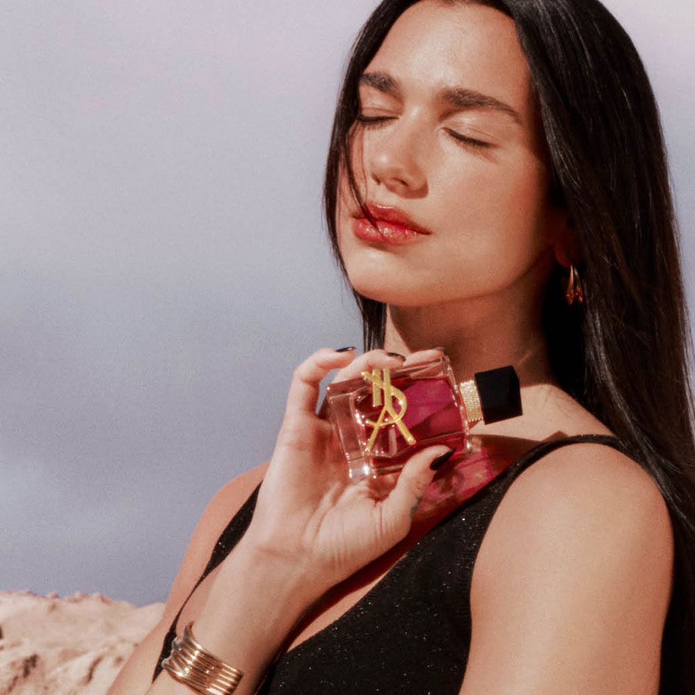 Dua Lipa con los ojos cerrados sosteniendo el perfume Libre Berry Crush en un desierto  