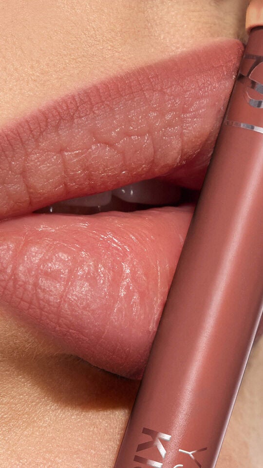 Labios de Adrienne con YSL LOVENUDE Kiss Shaper en el tono 103, un primer plano mostrando el producto.