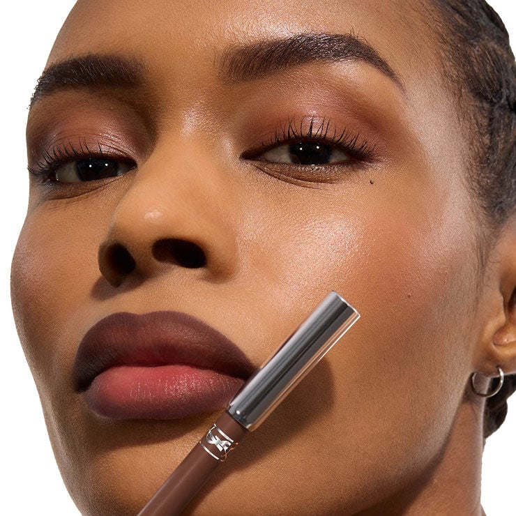 Modelo sosteniendo el perfilador YSL LOVENUDE KISS SHAPER con labios nude definidos.