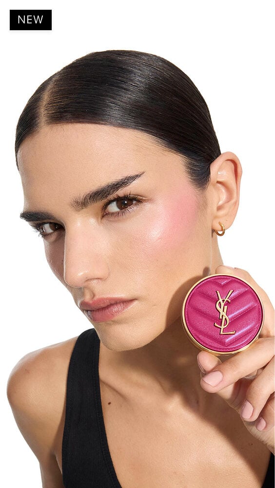 Iman, de tez media, sosteniendo un colorete en polvo fucsia YSL Make Me Blush en el tono 66, mostrando un rubor vibrante en su mejilla.
