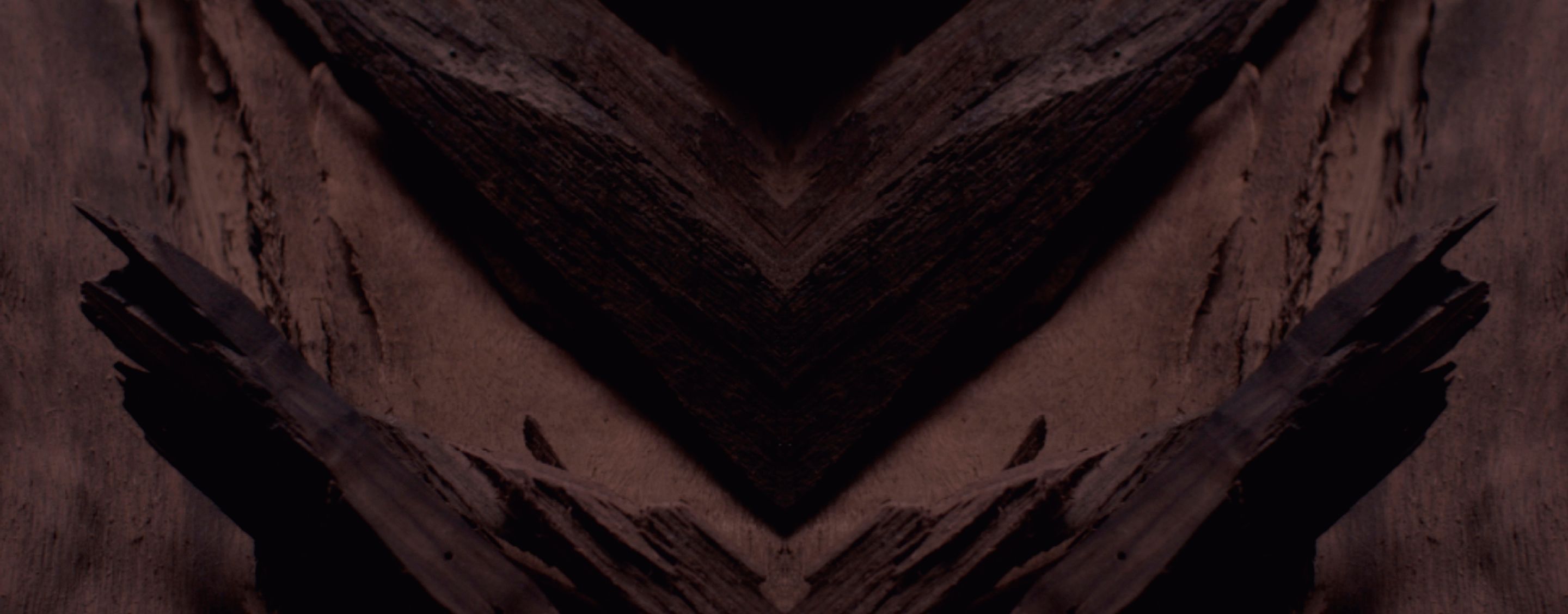 Dark, textured background with a prominent chevron pattern in deep browns and blacks, designed for YSL LVDP Extrait de Parfum product display.