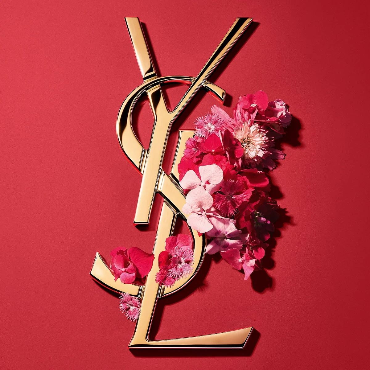 Dua Lipa holdsLibre Eau de parfum Berry Crush and a YSL Loveshine, with red lips and gold earrings.