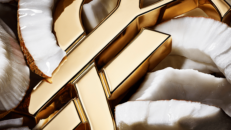Close-up of the gold YSL Cassandre logo surrounded by fresh coconut pieces, highlighting the creamy texture.