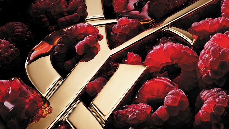Close-up of the gold YSL Cassandre logo surrounded by luscious red raspberries, emphasizing the fruity notes.