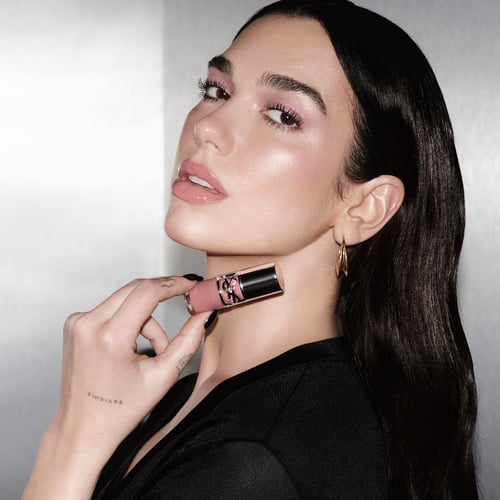 Dua Lipa sosteniendo un labial rosa de lujo cerca del mentón.