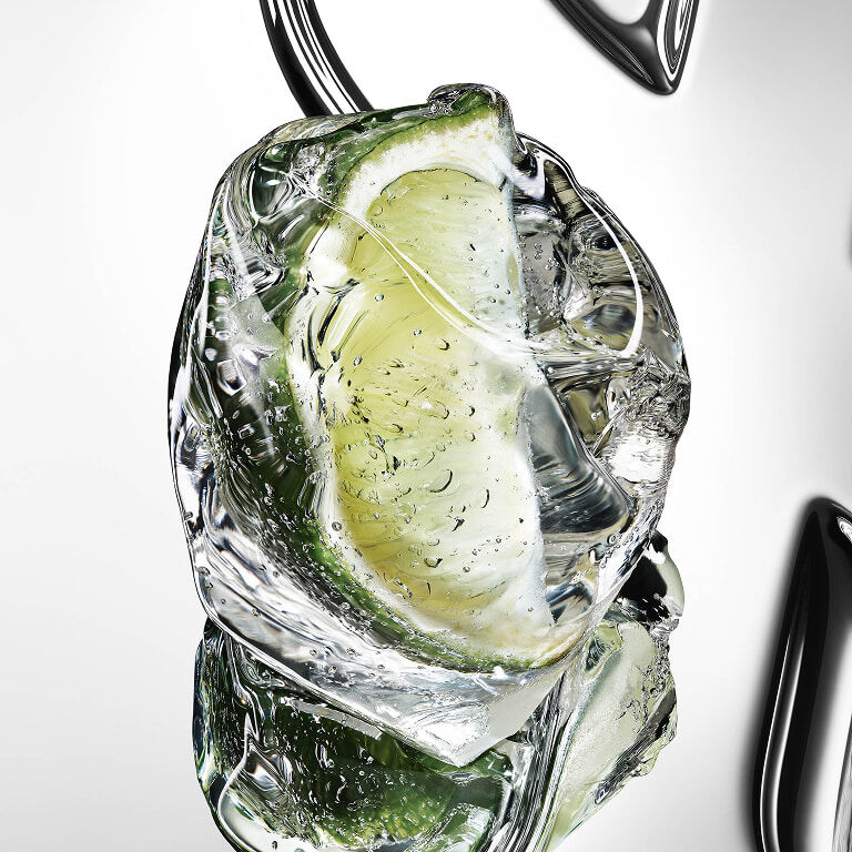Fresh green bergamot fruit cut in half with water droplets on a reflective YSL Cassandre
background.
