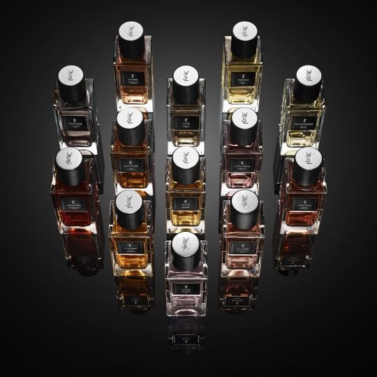 Colección de frascos de perfume YSL dispuestos sobre una superficie oscura y reflectante.